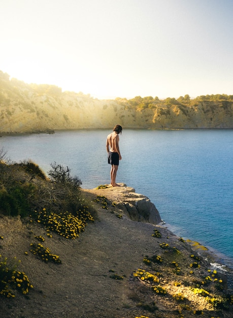 Pionowe ujęcie samotnego mężczyzny szykującego się do skoku do jeziora w słoneczny dzień