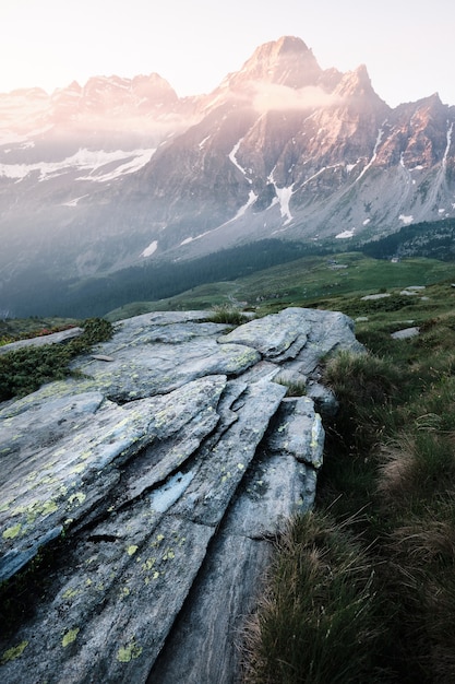 Bezpłatne zdjęcie pionowe ujęcie skały na trawiastym wzgórzu z górami