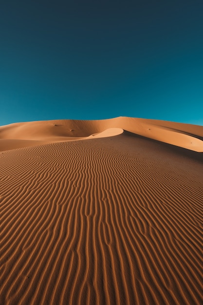 Pionowe ujęcie spokojnej pustyni pod czystym, błękitnym niebem uchwycone w Maroku