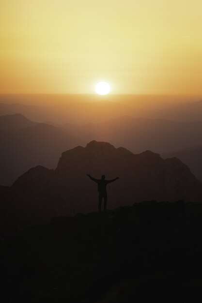 Pionowe ujęcie sylwetki męskiego turysty na szczycie góry patrzącego na zachód słońca