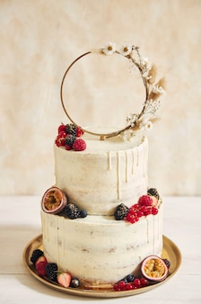 Pionowe ujęcie tortu weselnego ozdobionego świeżymi owocami i jagodami oraz pierścionkiem z kwiatów