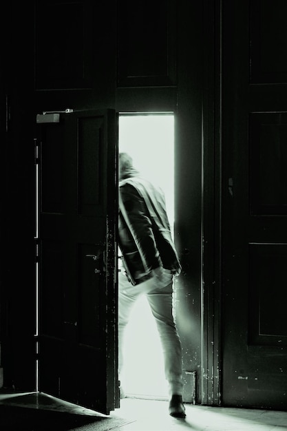 Pionowe ujęcie w skali szarości przedstawiające mężczyznę wychodzącego z pokoju z żelaznymi drzwiami