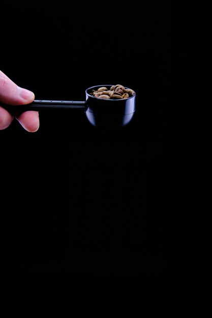 Pionowe ujęcie ziaren kawy w czerpaku kawy samodzielnie na czarnym tle