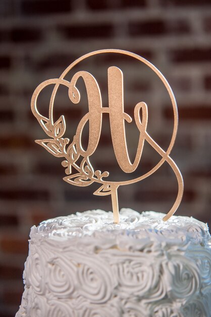 Pionowe zbliżenie strzał topping w kształcie litery H na piękny biały tort weselny