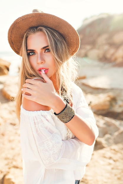 Pionowy portret atrakcyjna blondynka z długimi włosami, pozowanie do kamery na tle światła słonecznego na bezludnej plaży.