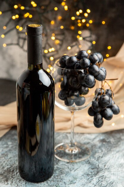 Pionowy widok butelki czerwonego wina i czarnego winogrona w szklance i ręczniku na ciemnym tle
