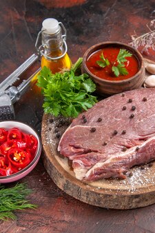 Pionowy widok czerwonego mięsa na drewnianej tacy i zielonego keczupu czosnkowego i posiekanej butelki oleju pieprzowego na ciemnym tle