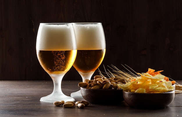 Piwo spienione z pistacjami, kłosy pszenicy, frytki w szklankach na drewnianym stole, widok z boku.