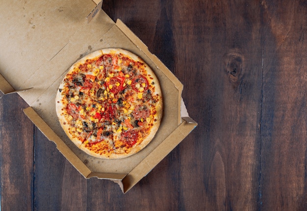 Pizza w pizzy pudełku na ciemnym drewnianym tle. leżał płasko.