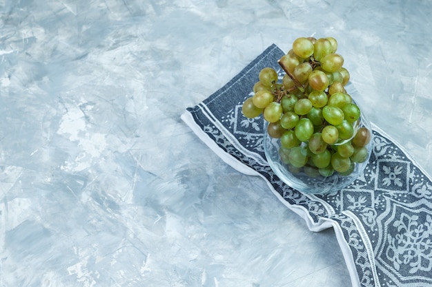 Bezpłatne zdjęcie płaskie leżały zielone winogrona w szklanym garnku na szarym tle nieczysty i ręcznik kuchenny. poziomy