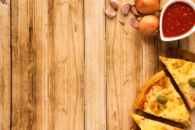 Bezpłatne zdjęcie plasterek pizzy i sos z surowego składnika na powierzchni drewnianych