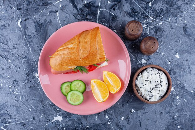 Plasterki cytryny i ogórka, kanapka na talerzu obok miski sera, na niebiesko.
