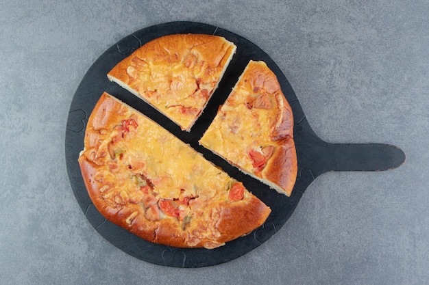 Plasterki domowej pizzy na czarnej desce do krojenia.