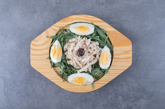 Bezpłatne zdjęcie plasterki kurczaka z jajkami i estragonem na drewnianym talerzu.