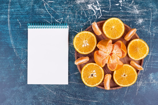 Plasterki pomarańczy i mandarynek na drewnianym talerzu z notatnikiem na boku. Wysokiej jakości zdjęcie