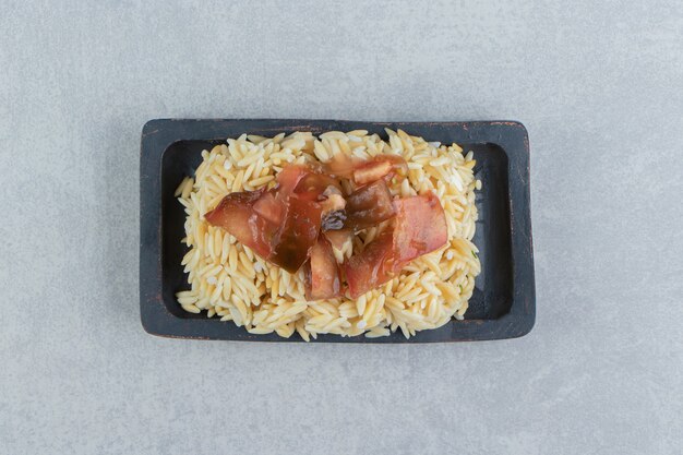Plasterki pomidorów na ryżowym drewnianym talerzu, na marmurowym tle.