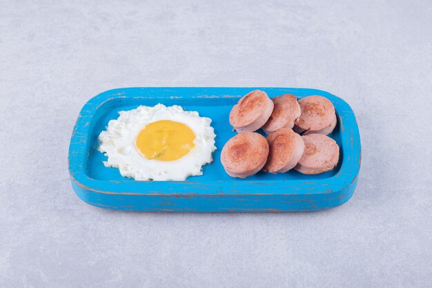 Plasterki smażone kiełbaski i jajko na niebieskim talerzu.