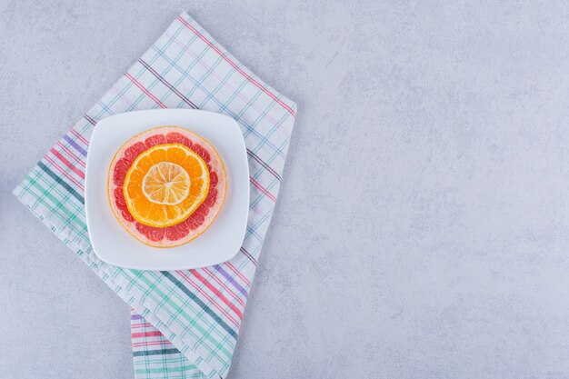 Plasterki świeżego grejpfruta, pomarańczy i cytryny na białym talerzu.