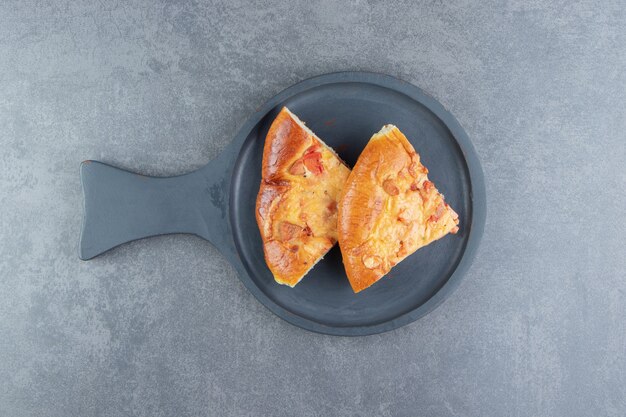 Plastry mieszanej pizzy na czarnej desce do krojenia.