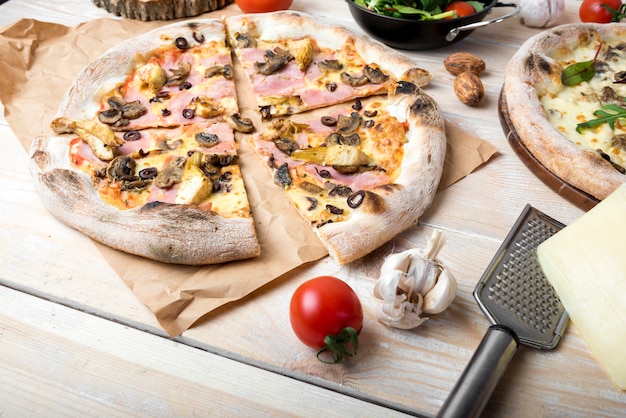 Plastry świeżej pizzy z dodatkami grzybowymi; pomidor wiśniowy; czosnek i ser na stole