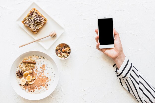 Płatki owsiane; dryfruits i plaster miodu na stole z telefon w rękach