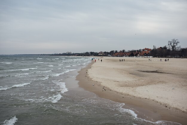 Plaża otoczona morzem i zabudowaniami pod zachmurzonym niebem w ciągu dnia