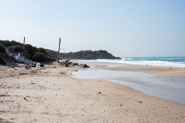 Plaża z ludźmi na niej otoczona morzem i wzgórzami pokrytymi zielenią w słońcu