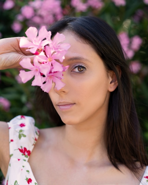 Płytkie ujęcie młodej brunetki rasy kaukaskiej z różowymi kwiatami w dłoni
