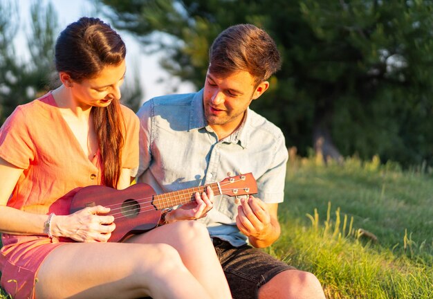 Płytkie ujęcie młodej pary grającej na ukulele w parku