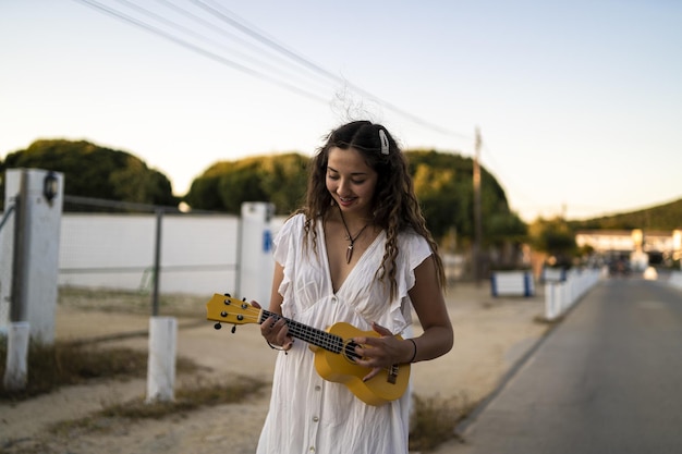 Bezpłatne zdjęcie płytkie ujęcie uśmiechniętej kobiety grającej na żółtym ukulele na poboczu drogi