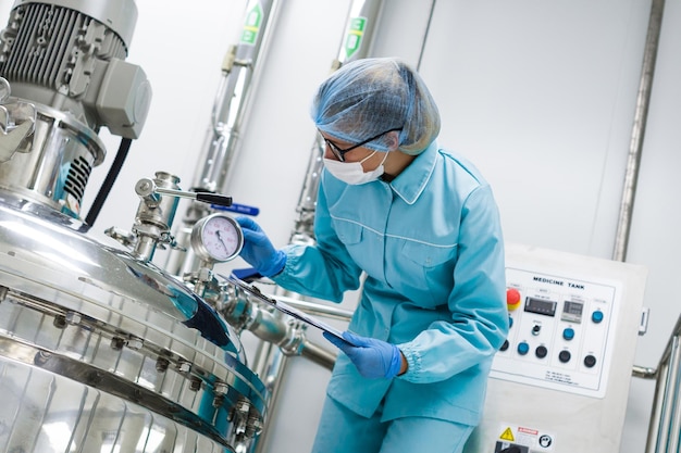 Bezpłatne zdjęcie pochylony naukowiec w niebieskim laboratoryjnym mundurze sprawdź jak działa kompresor, tablet w dłoniach z bliska
