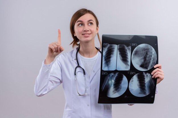 Pod wrażeniem młoda kobieta lekarz ubrana w szlafrok i stetoskop i trzymając strzał rentgenowski podnoszący palec