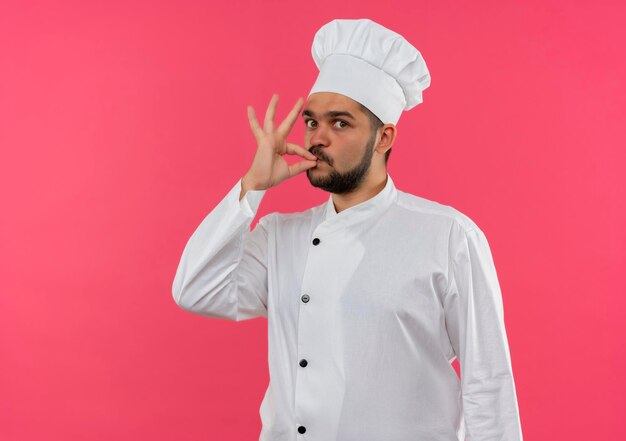 Pod wrażeniem młodego kucharza w mundurze szefa kuchni robi smaczny gest na różowej ścianie z miejscem na kopię copy