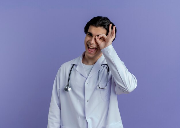 Pod wrażeniem młody mężczyzna lekarz ubrany w szlafrok medyczny i stetoskop patrząc robi wygląd gest na białym tle
