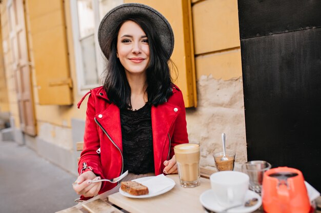 Podekscytowana brunetka kobieta w kapeluszu odpoczywa w kawiarni