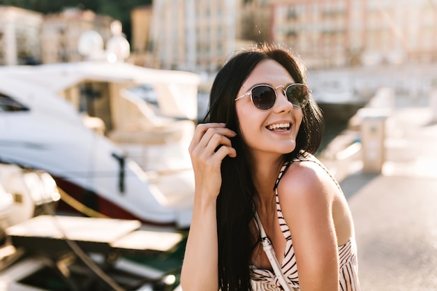 Bezpłatne zdjęcie podekscytowana dziewczyna z długimi czarnymi włosami szczęśliwa śmiejąc się siedząc na świeżym powietrzu z łodziami