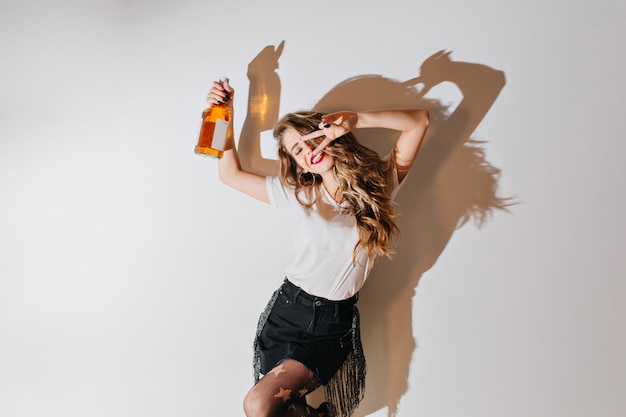 Bezpłatne zdjęcie podekscytowana kobieta tańczy z butelką koniaku z kręconymi fryzurami