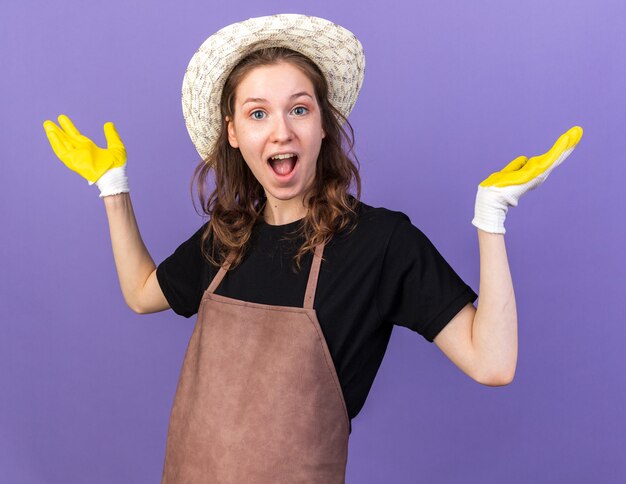 Podekscytowana młoda kobieta ogrodniczka w kapeluszu ogrodniczym z rękawiczkami rozkładającymi ręce