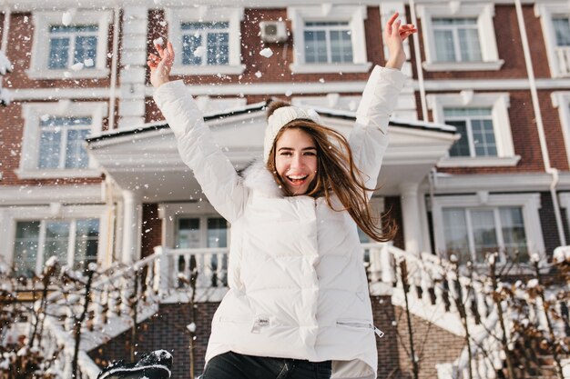 Podekscytowane jaskrawe emocje radosnej ładnej młodej kobiety na ulicy w okresie zimowym. Podnoszenie rąk, szczęście, pozytywność, radość, ferie zimowe.