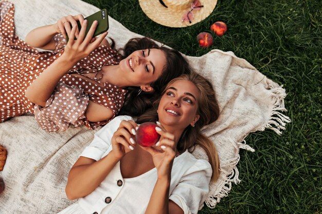 Podekscytowane młode panie w letnich strojach urządzają sobie piknik na zielonej trawie