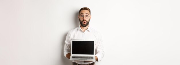 Podekscytowany biznesmen pokazujący coś na ekranie laptopa stojący szczęśliwy na białym tle