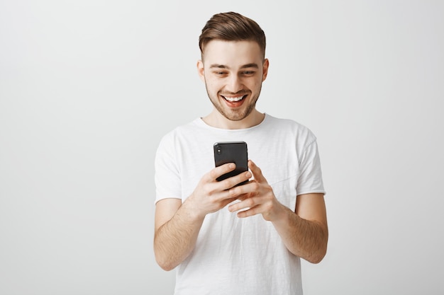 Podekscytowany szczęśliwy człowiek uśmiecha się do ekranu smartfona, za pomocą aplikacji na telefon komórkowy