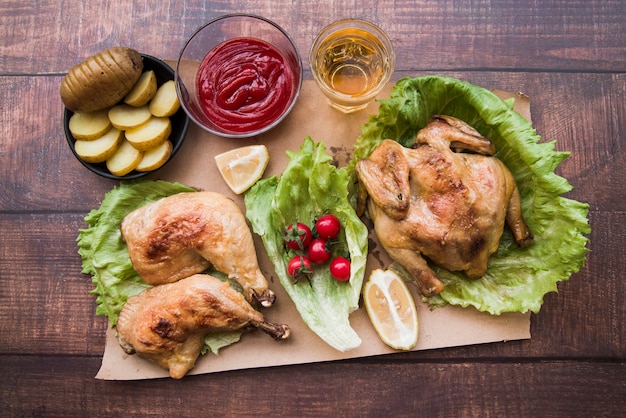 Bezpłatne zdjęcie podniesiony widok pieczonego kurczaka na kolację z piwem; plasterki ziemniaków; cytryna i sos na brązowym papierze
