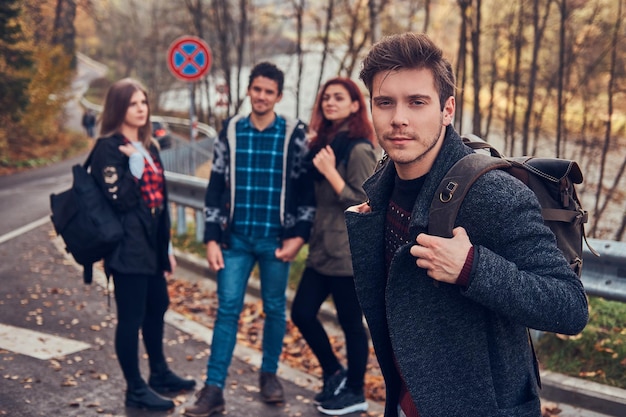Podróże, autostop, koncepcja przygody. Grupa młodych turystów stojących na uboczu drogi w pięknym lesie jesienią.