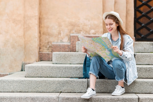 Bezpłatne zdjęcie podróżnik trzyma mapę i siedzi na widoku z przodu schodów