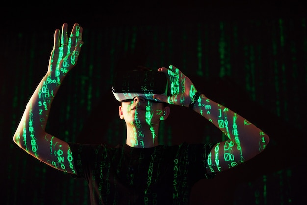 Podwójna ekspozycja kaukaskiego mężczyzny i zestawu słuchawkowego VR VR to prawdopodobnie gracz lub haker, który włamuje kod do bezpiecznej sieci lub serwera, z liniami kodu w kolorze zielonym