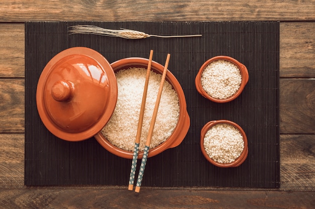 Podwyższony widok chopsticks nad uncooked ryżem rzuca kulą na drewnianym tle