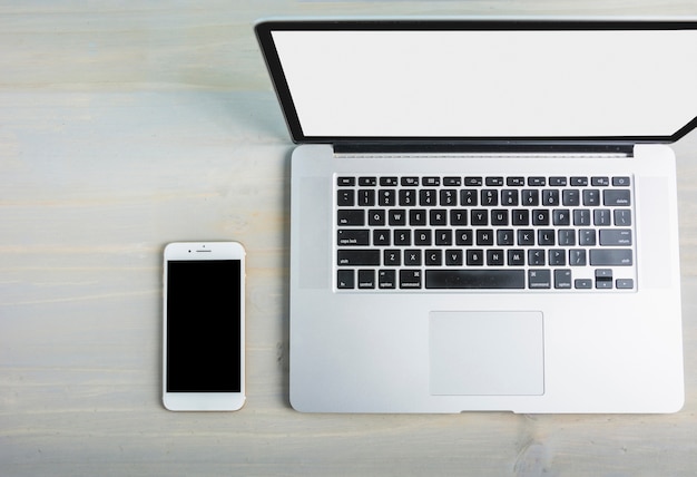 Podwyższony widok laptop z pustym bielu ekranem i telefonem komórkowym na drewnianym biurku