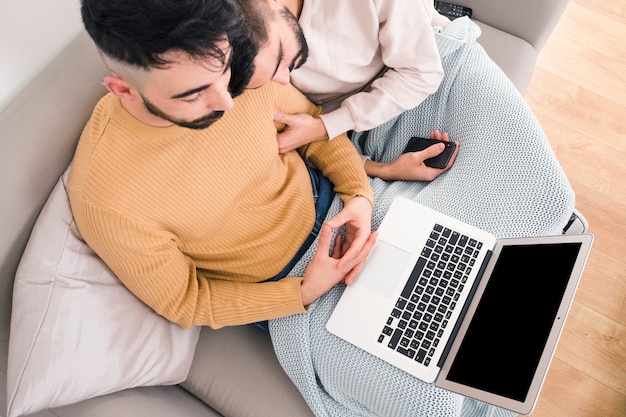 Podwyższony widok młody homoseksualny pary obsiadanie na kanapie patrzeje cyfrową pastylkę