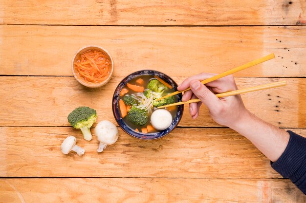 Podwyższony widok osoby jedzącej warzywa pałeczkami na drewnianej desce